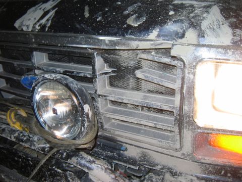 1985 Ford Bronco - Close-up of the front grille and headlight assembly on a 1985 Ford Bronco, showing damage and dirt.