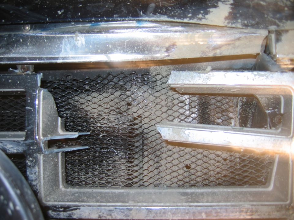 Close-up of chrome grille with black mesh screen, dusty and worn