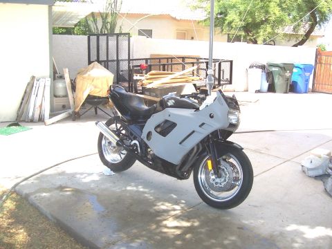 1994 Ford Bronco - A motorcycle with unpainted fairings sits in a driveway, with construction materials and trash cans in the background.