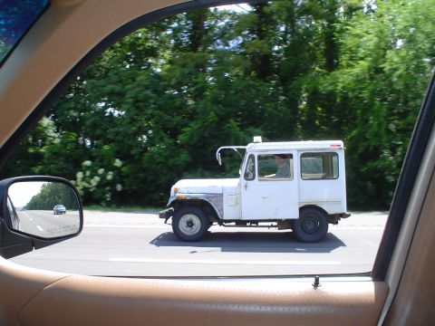 1981 Ford Bronco - A white panel van travels down the highway, viewed from the passenger side window of another car.