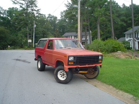 1981 Ford Bronco - This red SUV is parked on a street with houses and trees in the background.