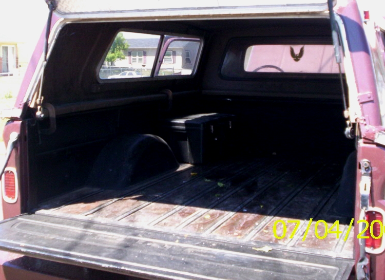 Open tailgate view into maroon pickup bed under camper shell with black storage box inside