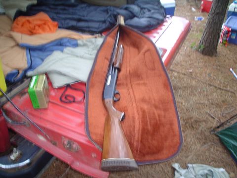 1981 Ford Bronco - A shotgun in its case rests on the tailgate of a red vehicle, surrounded by camping gear.