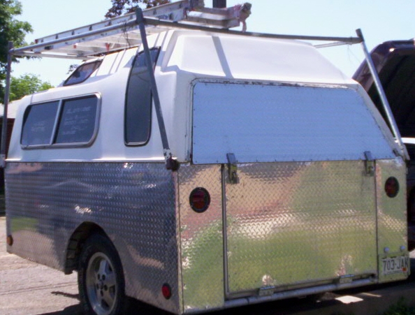Rear view of a diamond-plate aluminum camper trailer with white shell, ladder rack, and Colorado plate 703-JAN