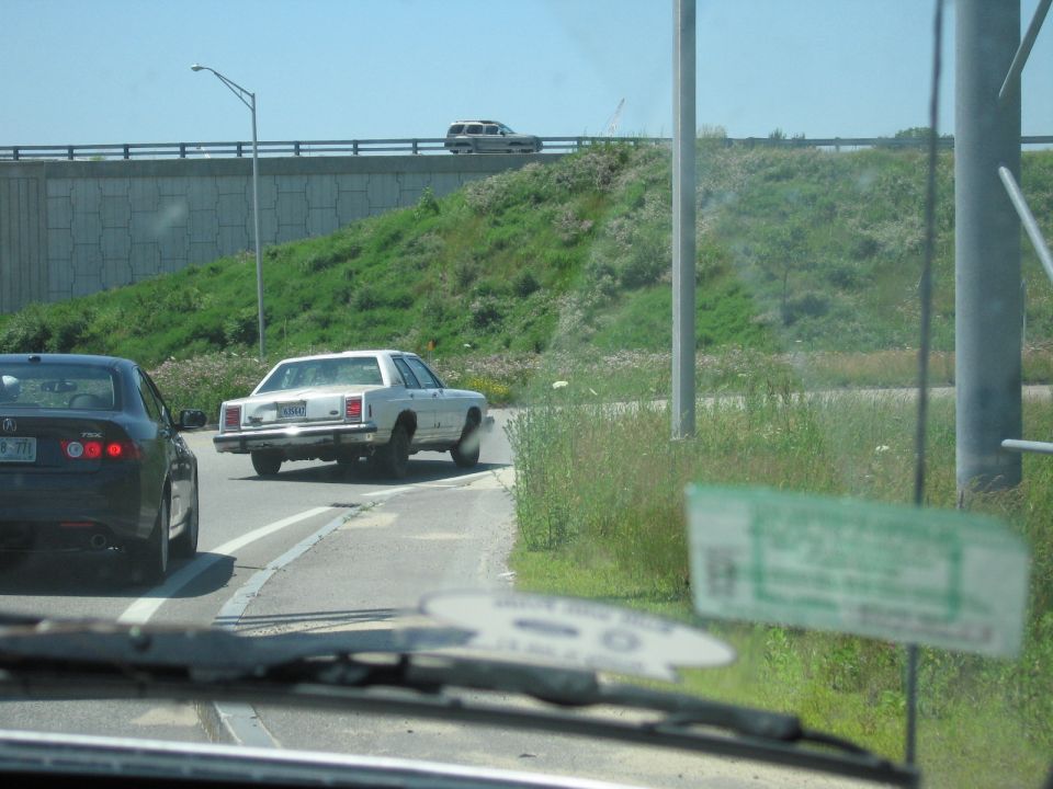 White boxy Ford sedan stopped on highway shoulder with rear wheel splayed outward
