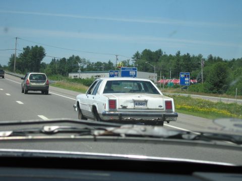 1991 Ford LTD Crown Victoria - Rear view, shot through a following car's windshield, of a weathered white Ford LTD Crown Victoria box sedan driving in the right lane of a…