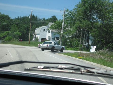 1991 Ford LTD Crown Victoria - Rear three-quarter view, shot through another vehicle's windshield with the wiper in frame, of a white Ford LTD Crown Victoria box-body sed…
