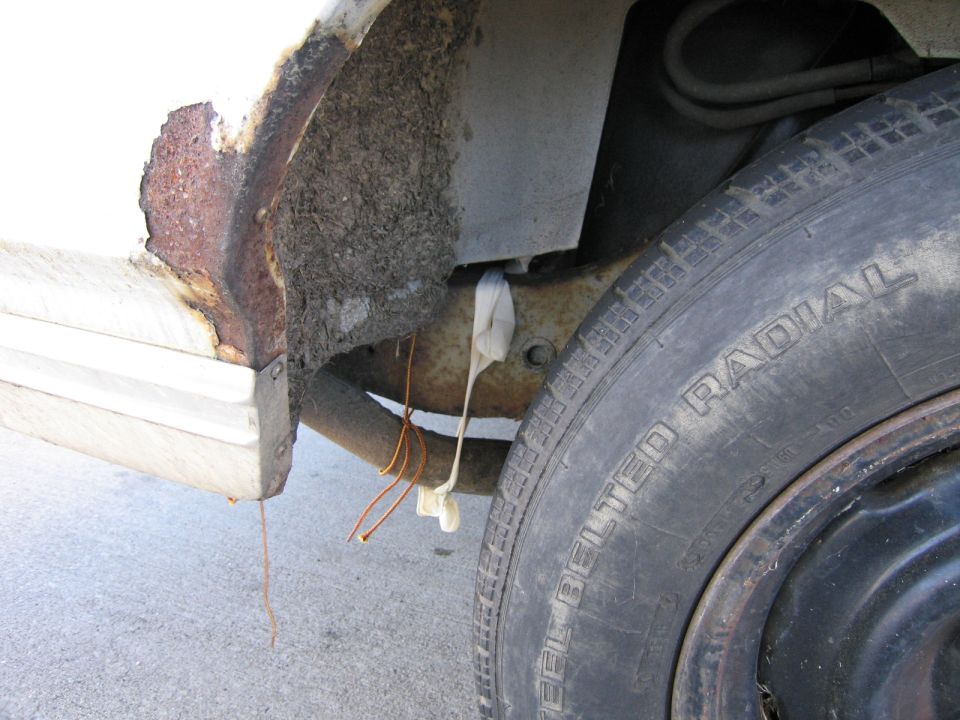 Rusted-through rear wheel arch on a white car above a black steel wheel