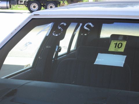 1991 Ford LTD Crown Victoria - Rear side window of a light-colored sedan on a dealer or lot, with "AS IS" hand-painted in white on the glass and a yellow New Hampshire Oc…