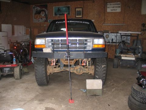 1995 Ford Bronco - A dark blue Ford Bronco is parked in a garage, modified for off-road use with a jack positioned in front of it.