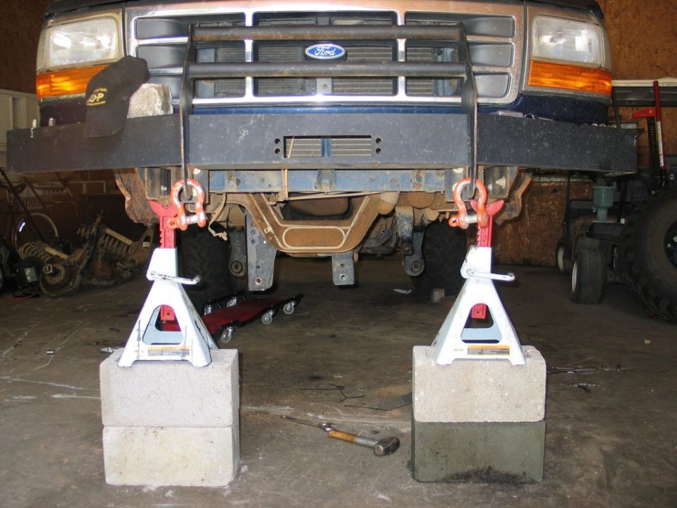Blue Ford truck front lifted on jack stands stacked on cinder blocks, undercarriage exposed