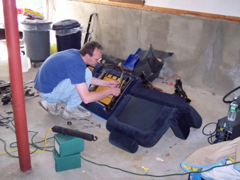 2001 Ford Crown Victoria - Disassembled car seat with a man working on its internal mechanisms.