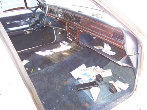2001 Ford Crown Victoria - The interior of a car shows a messy floor with papers and a walkie-talkie scattered around.