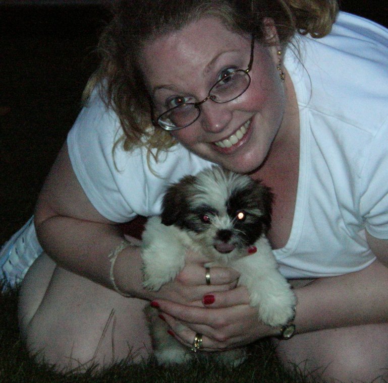 Woman with glasses holding a small shih tzu puppy. Supermotors logo in corner