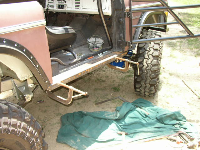 Brown Ford Bronco with roll cage, large off-road tires, and custom side bars. Interior visible