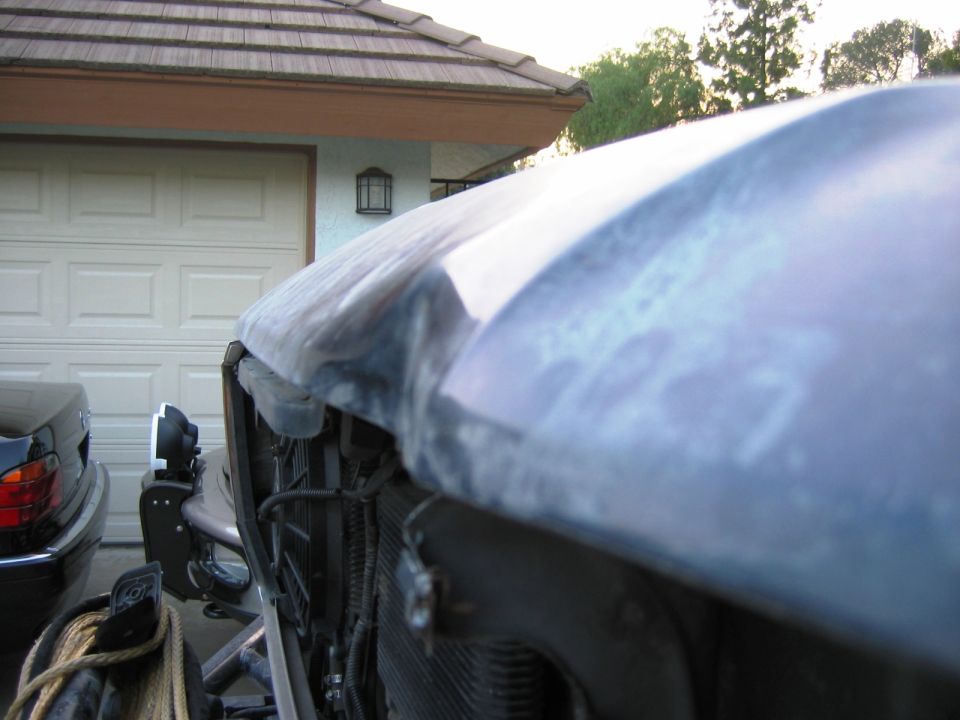 Front corner of primer-gray vehicle with exposed grille and winch in a driveway
