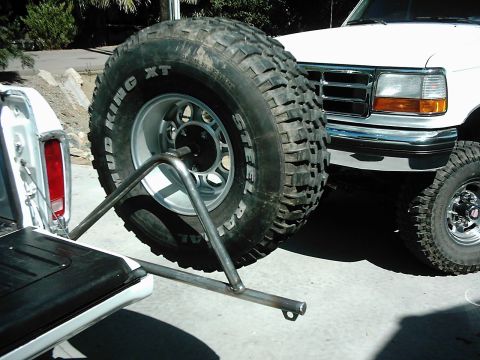 1978 Ford Bronco - A white truck's rear bumper is visible with a large spare tire mounted on a custom metal carrier.
