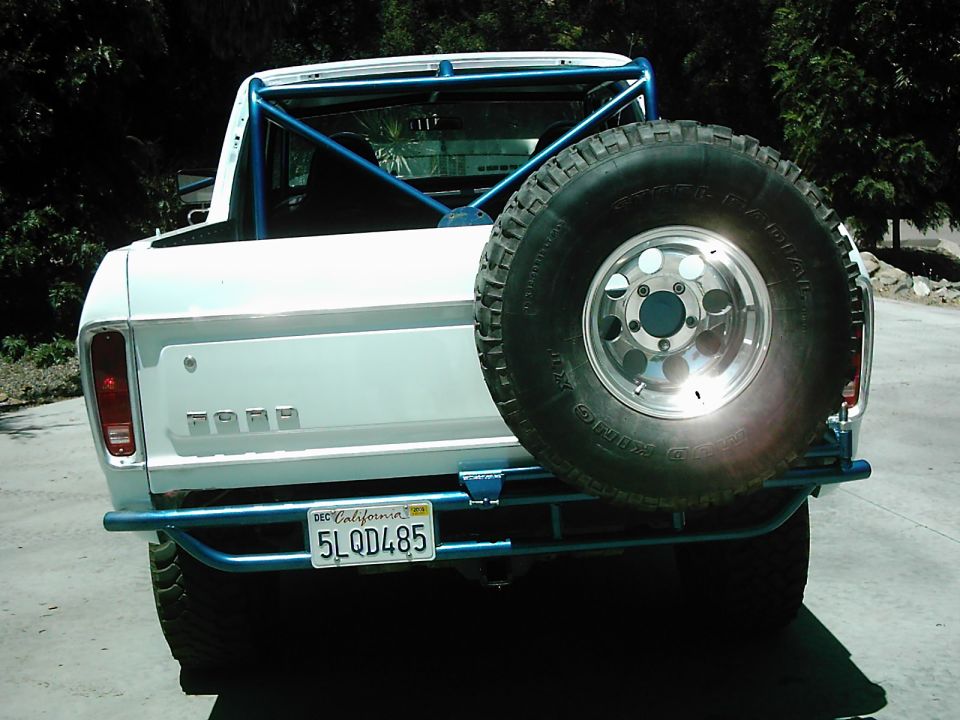 Rear view of a white 1978 Ford Bronco with a blue roll cage and spare tire carrier