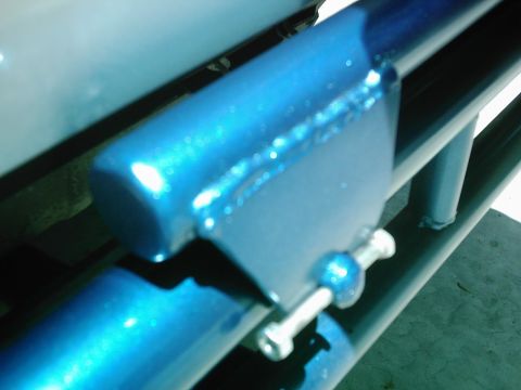 1978 Ford Bronco - This metallic blue bracket is attached with a bolt and nut, likely part of a vehicle's spare tire carrier system.