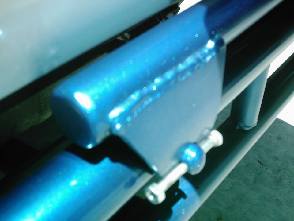 Close-up of a blue metallic bracket with a bolt and nut, part of a spare tire carrier