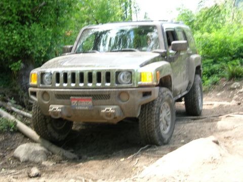 1989 Dodge Power Ram - A brown Hummer H3 navigates a rocky, wooded trail with mud on its exterior.
