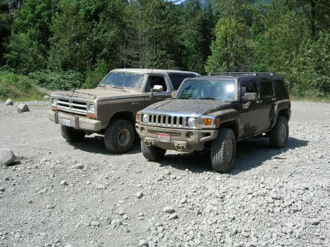 1989 Dodge Power Ram - Two off-road vehicles, a 1989 Dodge Power Ram and a Hummer H3, are parked on a gravel surface with trees in the background.