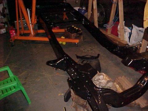 1979 Ford F-250 - The bare frame of a vehicle is suspended from an engine hoist, undergoing restoration work.