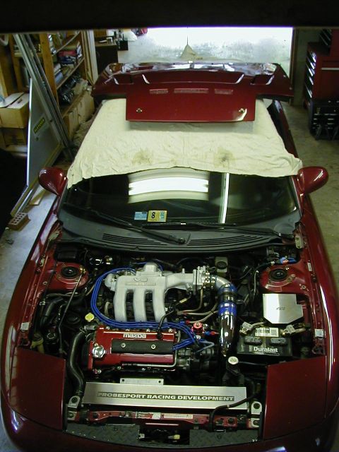 1994 Ford Probe - The engine bay of a red Mazda is visible with the hood open, revealing the engine and various components.