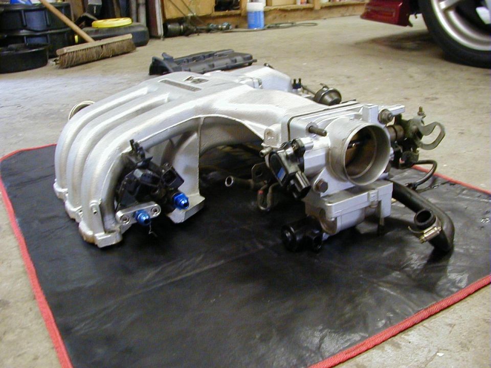 Silver aluminum intake manifold with throttle body and sensors removed from a vehicle