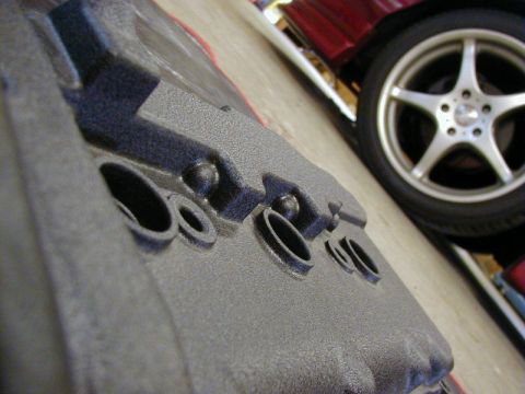 1994 Ford Probe - A textured engine component is shown in the foreground, with a portion of a red vehicle and its silver wheel visible behind it.