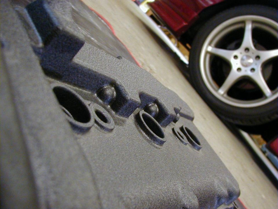 Close-up of a textured engine part with a silver five-spoke wheel and red car body in the background