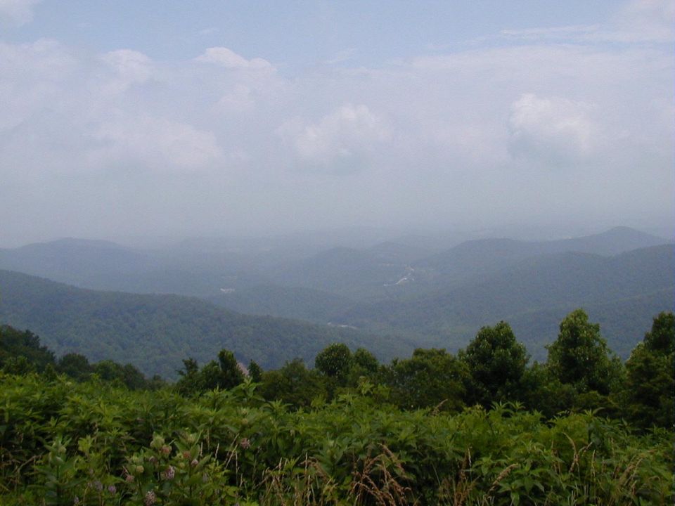 Hazy mountain range with green trees in the foreground and a cloudy sky