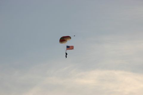 2003 Jeep TJ - A skydiver carries an American flag while descending under a parachute against a pale blue sky.