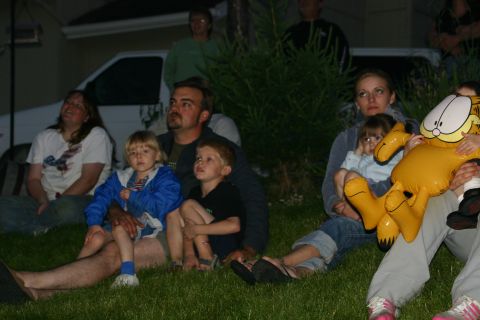 2003 Jeep TJ - A group of people, including children and an adult holding a Garfield balloon, sit on the grass at dusk, seemingly watching an event.