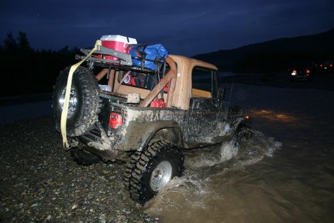 2003 Jeep TJ - A heavily modified Jeep Wrangler navigates a shallow river at twilight, equipped for off-road adventure.