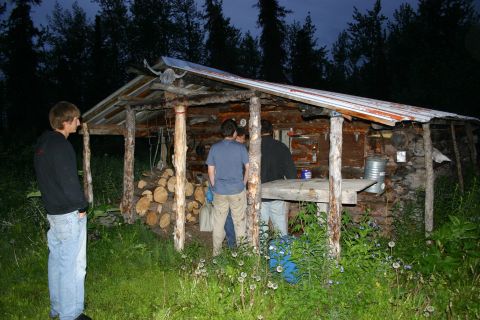 2003 Jeep TJ - A group of people gathered around a rough-hewn cabin in a wooded area at dusk.