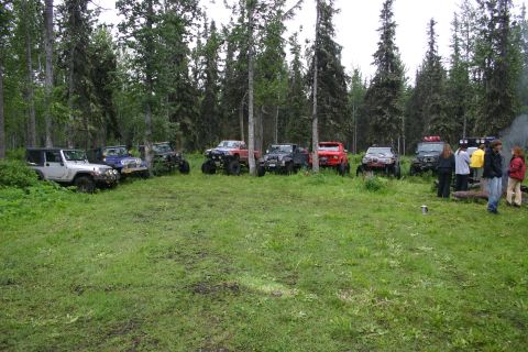 2003 Jeep TJ - A group of off-road vehicles are parked in a clearing surrounded by trees, with several people standing nearby.