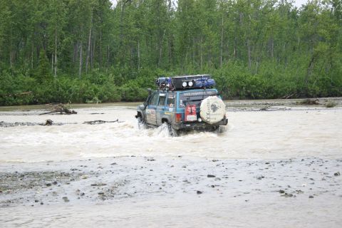 2003 Jeep TJ - SUV navigates a river crossing with trees in the background.