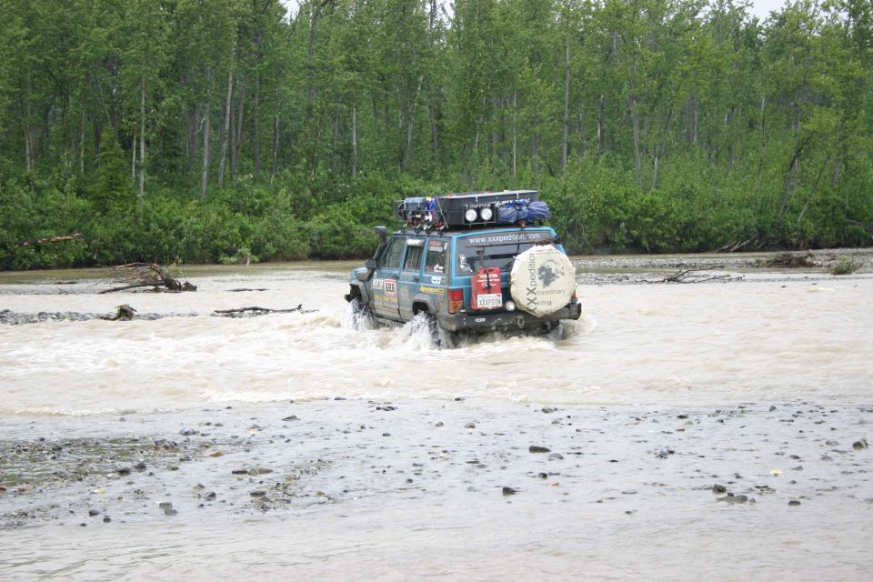 Blue SUV with roof rack and spare tire cover driving through a river