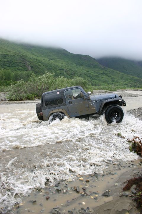 2003 Jeep TJ - 2003 Jeep TJ navigating a river crossing with terrain and misty mountains.