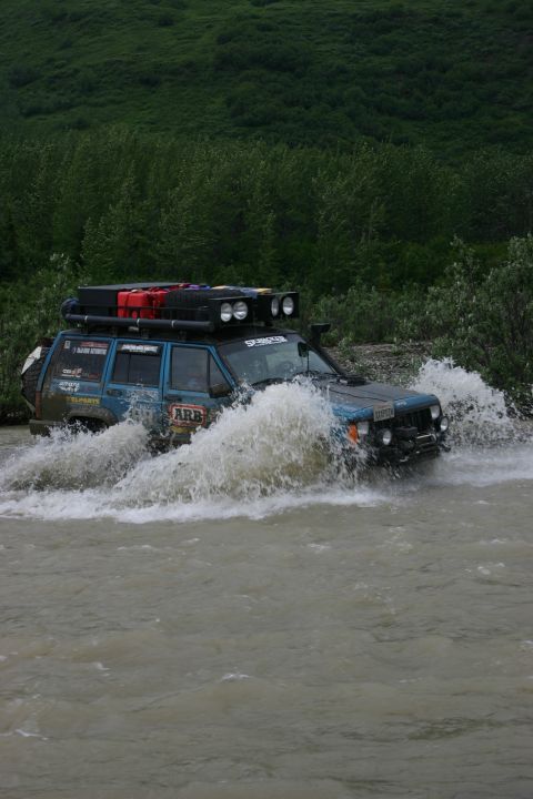 2003 Jeep TJ - This modified Jeep Cherokee XJ navigates a water crossing, kicking up a large spray.