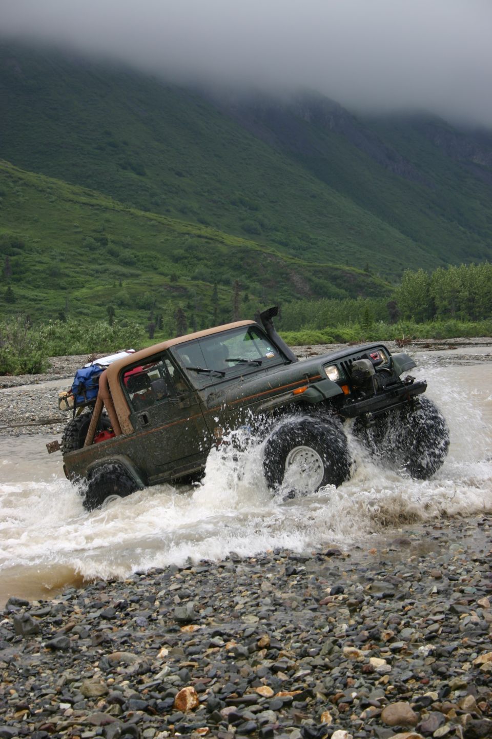 Green 2003 Jeep TJ driving through river with large tires