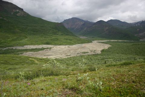 2003 Jeep TJ - A vast, green mountain valley stretches under a cloudy sky, with a wide, sandy riverbed cutting through the landscape.