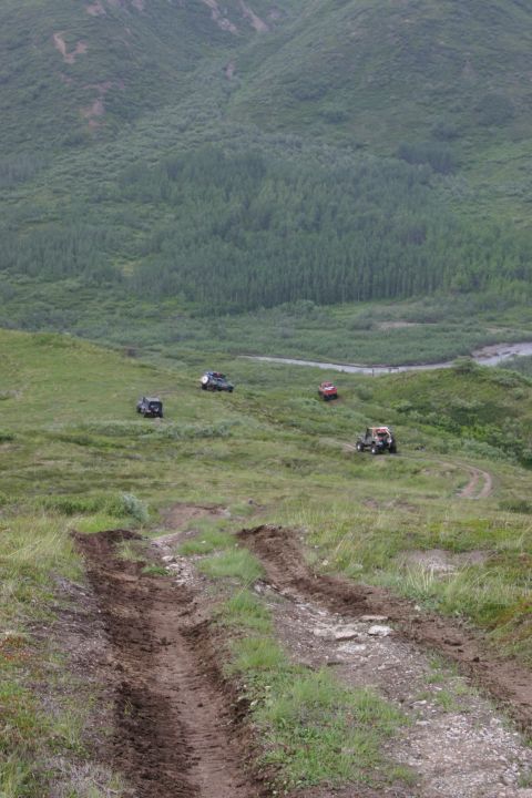 2003 Jeep TJ - Multiple off-road vehicles navigate a challenging grassy hillside with a wooded valley in the background.
