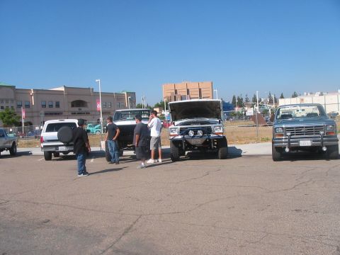 1986 Ford Bronco - Several vehicles are parked in a lot under a clear blue sky, with buildings in the background.