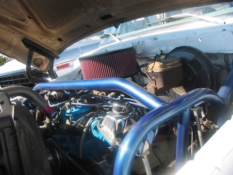 1986 Ford Bronco - The engine bay of a vehicle features a blue roll cage and a red air filter, with another vehicle partially visible in the background.