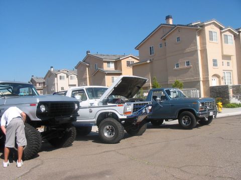 1986 Ford Bronco - Three pickup trucks are parked on a street in front of houses. The truck on the right is a 1979 Ford F-150.