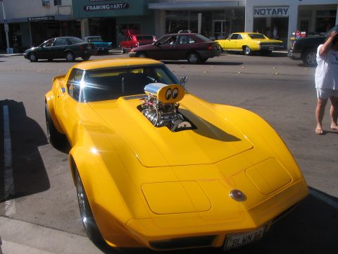 1986 Ford Bronco - A bright yellow 1975 Chevrolet Corvette is parked on a street, a large supercharger with cartoon eyes on its hood.