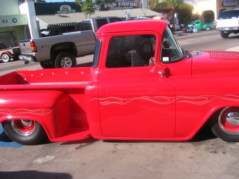 1986 Ford Bronco - A classic red pickup truck with flame decals is parked on a street, with other vehicles in the background.