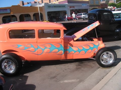 1986 Ford Bronco - An orange hot rod with blue flame decals is parked on a street with its hood open.